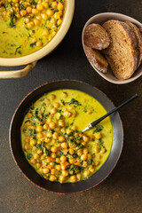 Healthy tasty lunch, soup with chickpeas and spinach, with spices and fresh herbs, with coconut milk on a brown background, top view