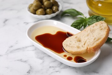 Bowl of organic balsamic vinegar with oil served with bread slice, basil and olives on white marble table. Space for text