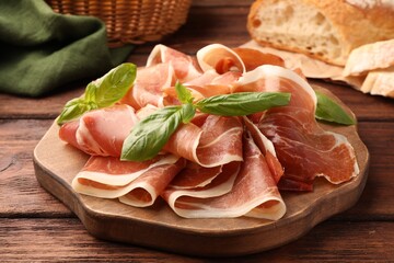 Slices of tasty cured ham and basil on wooden table, closeup