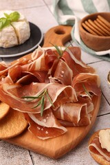 Slices of tasty cured ham, crackers and rosemary on tiled table, closeup