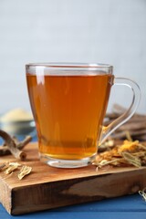 Aromatic licorice tea in cup and dried sticks of licorice root on blue wooden table, closeup