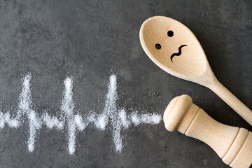 Salt shaker, wooden spoon, cardiogram made of salt, unhealthy cooking and hypertension concept