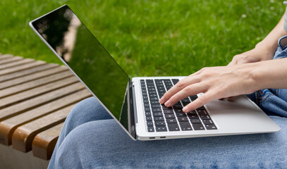 Young woman using laptop computer in park, freelance student girl working and studying online outdoors