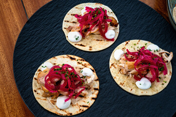 Enjoy an elegant dish of petite pita bread filled with succulent chicken slices, tangy pickled onions, and delightful quail eggs. 3 pieces on a black dish.