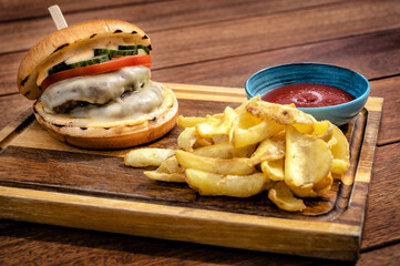 Cheeseburger feast on a rustic wooden board.  Juicy burger topped with melted cheese, crisp lettuce, ripe tomatoes, pickles. Alongside portion of golden, crispy french fries and ketchup sauce.