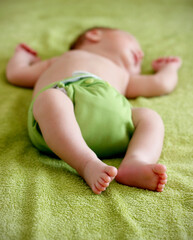 Close up of cute bare feet of 1-month old baby wearing green cloth diaper and sleeping on green towel in bed. Eco friendly reusable baby diaper. Sustainable life, zero waste concept.
