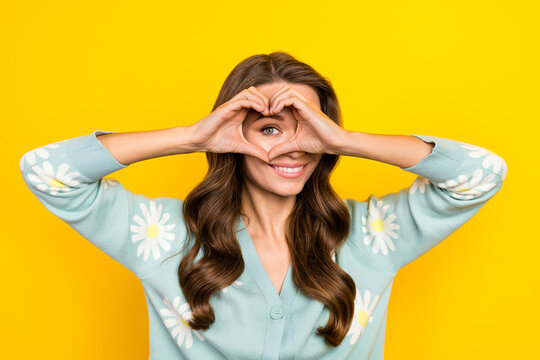 Portrait of pretty cheerful person eye watch look through arms demonstrate heart gesture isolated on yellow color background