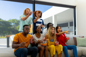 Group of focused diverse friends sitting on sofa, watching sport of tv