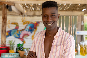 Fototapeta premium Portrait of happy biracial man standing in sunny beach bar smiling, unaltered