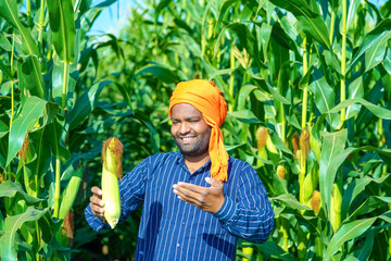 young indian farmer showing corn at corn field.