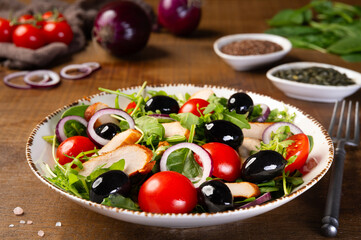 Fototapeta na wymiar Salad with grilled chicken fillet meat, fresh vegetables, spinach, arugula (ruccola), red onion, cherry tomato and olives. Healthy menu. Diet food. Wooden background.