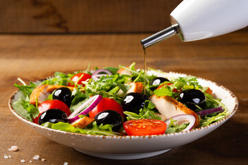 Salad with grilled chicken fillet meat, fresh vegetables, spinach, arugula (ruccola), red onion, cherry tomato and olives. Healthy menu. Diet food. Wooden background.