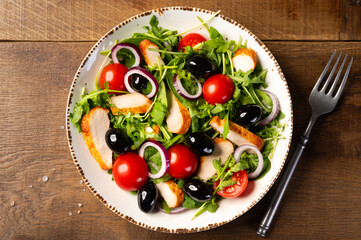 Salad with grilled chicken fillet meat, fresh vegetables, spinach, arugula (ruccola), red onion, cherry tomato and olives. Healthy menu. Diet food. Wooden background. Top view.