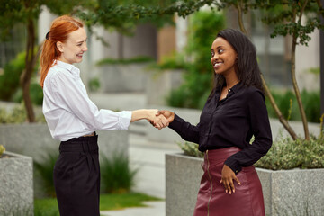 Future cooperation and partnership. Two women, employees standing outside and shaking hands. Successful teamwork