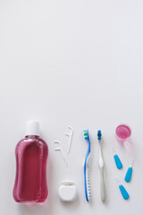 Flatlay of dental floss, toothbrushes, toothpicks and rinse on white with copyspace