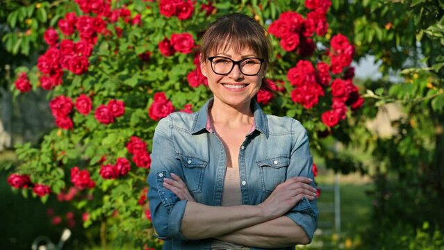 Portrait of middle-aged woman in backyard, background blooming red rose bush