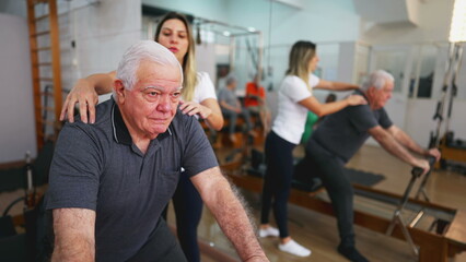 Fototapeta na wymiar Senior Man Exercising in Guided Workout, Pilates Studio Session with Female Coach, elderly person using machine to stretch, taking care of spine health