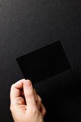 Vertical image of hand of caucasian woman with business card with copy space on black background