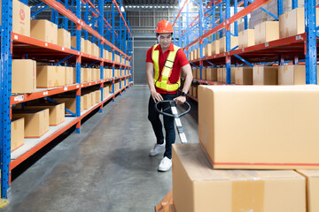 Young man pulling hand pallet truck loading package boxes stacked in shipping warehouse. Asian worker moving merchandise from storage shelf by hand lift pallet jack. Delivery goods, cargo transport.