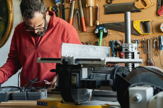 Carpenter working with power and hand tools. Carpenter working with power and hand tools. Man with beard and glasses working in a small bussiness workshop
