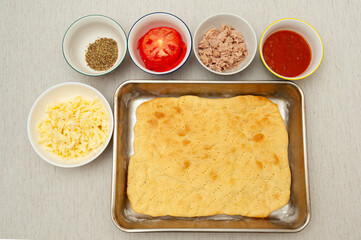 Making Homemade Rectangular Pizza - Ingredients in top view: Cheese, oregano, tomato, tuna, sauce;...