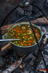a camp pot hangs over the fire on a tripod. Cooking on a camping trip, hiking