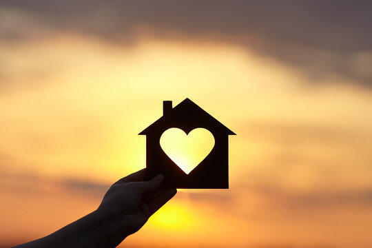 Hand holds wooden house in the form of heart against the sun