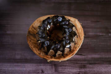 chocolate cupcake decorated with blueberries with icing on a wooden birch stand, on a dark background