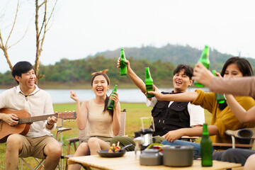 Group of Asian young adult people enjoy drinking a beer together during camping at the park. Asian young women and men celebrating with a bottle of a beer together.