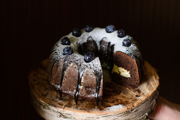 chocolate cupcake with blueberries on a birch wooden saw cut, with a piece cut off, and cream inside, on a dark background