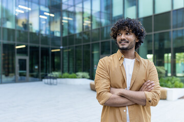 Portrait of an Indian young man, confident businessman, office worker standing outside an office...
