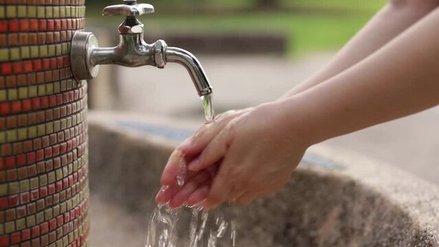 夏の公園で水道水を使って手洗いしている女性の両手の様子