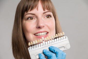 Close-up of dentist using shade guide at woman's mouth to check veneer of teeth for bleaching