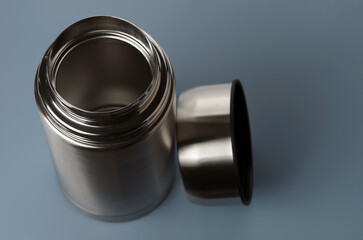 Empty stainless-steel vacuum flask with lid removed on a blue-grey  background. Selective focus.