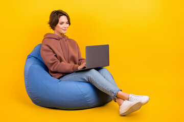 Full length cadre of young charming girl brown hair wear sweatshirt use netbook apple online conference isolated on yellow color background
