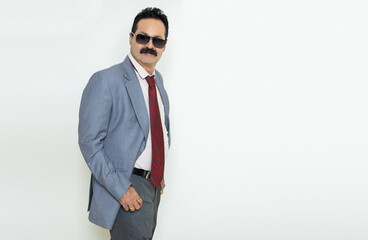 Mature indian businessman wearing suit and sunglasses standing with his hands in pocket isolated over white background. Corporate Concept.