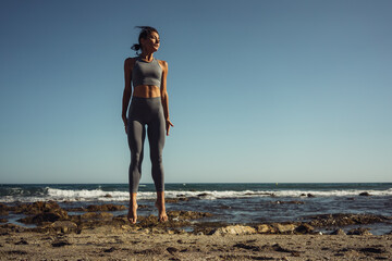 a beautiful brunette girl in gray leggings is engaged in fitness on the sand against the background of the sea