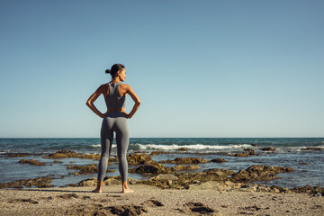 Fototapeta na wymiar a beautiful brunette girl in gray leggings is engaged in fitness on the sand against the background of the sea