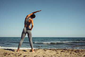 a beautiful brunette girl in gray leggings is engaged in fitness on the sand against the background of the sea