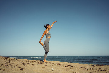 a beautiful brunette girl in gray leggings is engaged in fitness on the sand against the background of the sea
