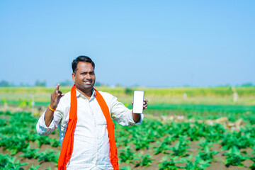 Young indian showing smartphone at brinjal farm field.