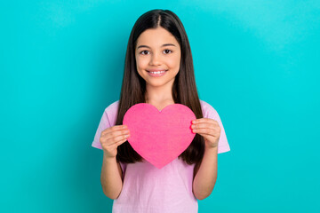 Photo of dreamy attractive little child dressed pink t-shirt rising paper heart isolated teal color...