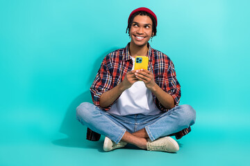 Full body portrait of positive minded man sit floor hold smart phone look interested empty space...