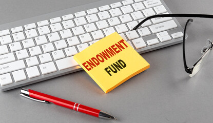 ENDOWMENT FUND text on a sticky with keyboard, pen glasses on grey background