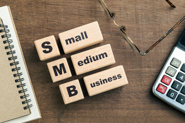 SMB, Small and medium business text on wood blocks on the desk, with part of calculator, eyeglasses...