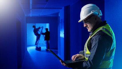 Man builder with laptop. Engineer in parietal corridor. Foreman supervises work of electricians....