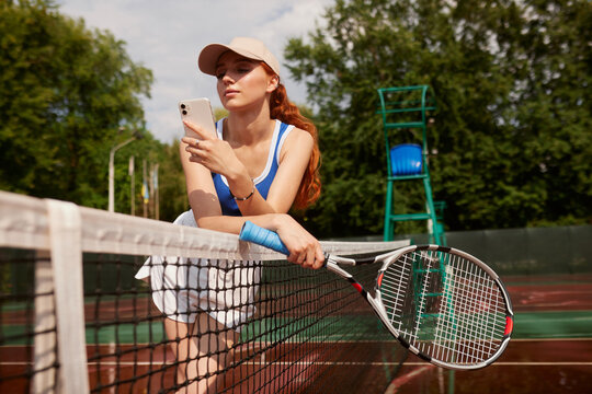 Active, fit and happy female tennis player browsing social media on her phone outdoors on the court. A young female athlete or sportswoman posting her sport training online or on the internet