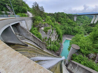 Water flowing over spillway of a hydroelectric dam, highway bridge in background