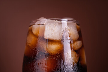 Cola with ice. Fresh cold sweet drink with ice cubes. Over brown background with copy space. Cola...