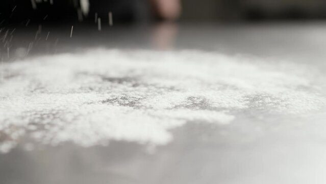 Sprinkle with flour on a black background. Close-up of a young housewife's hand sprinkling flour on the table. The cook makes flour for baking on the table. The cook sprinkles the table with flour for